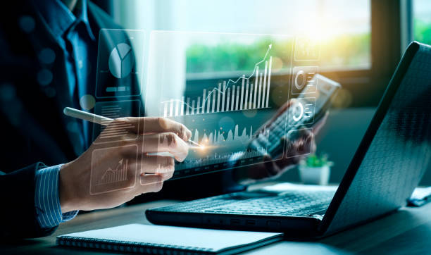 Businessman analyzing data on digital graphs while using a laptop, representing hidden costs in RAK Free Zone licenses.