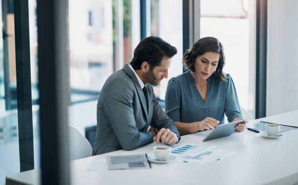 Two professionals review hidden costs on a tablet while discussing licensing in a modern office setting.